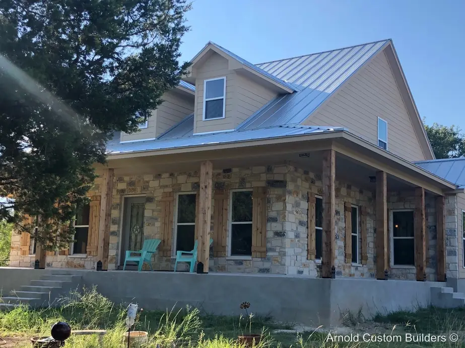 A Texas hill country stone farmhouse with a covered porch and cedar posts, built by Arnold Custom Builders