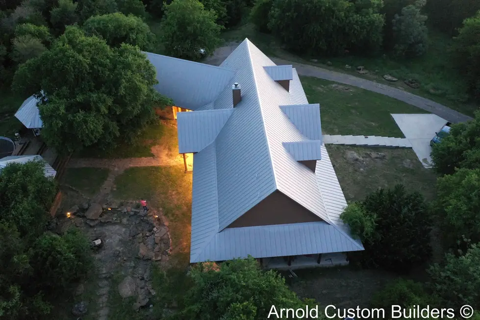 Twilight aerial photograph of a home with a standing seam roof and multiple dormers