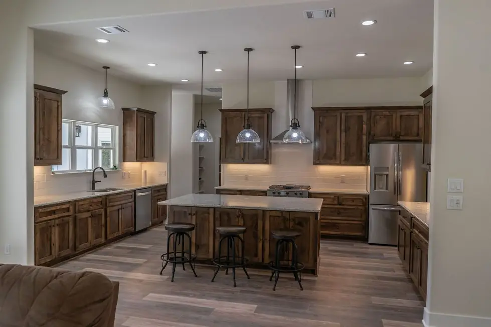 A warm rustic kitchen with stained knotty alder cabinetry, stone countertops and industrial bar stools