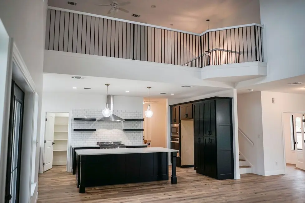 A kitchen with black cabinetry, white subway tile, a stainless range hood and open shelving