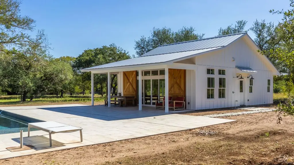 A detached pool house and cabana with barn doors and a covered patio beside an in ground pool